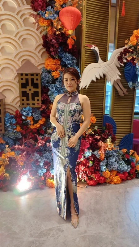 Wanita cantik mengenakan Cheongsam lengan pendek motif bunga warna gold berlatar biru navi. Cheongsam dibuat oleh Fifilia.