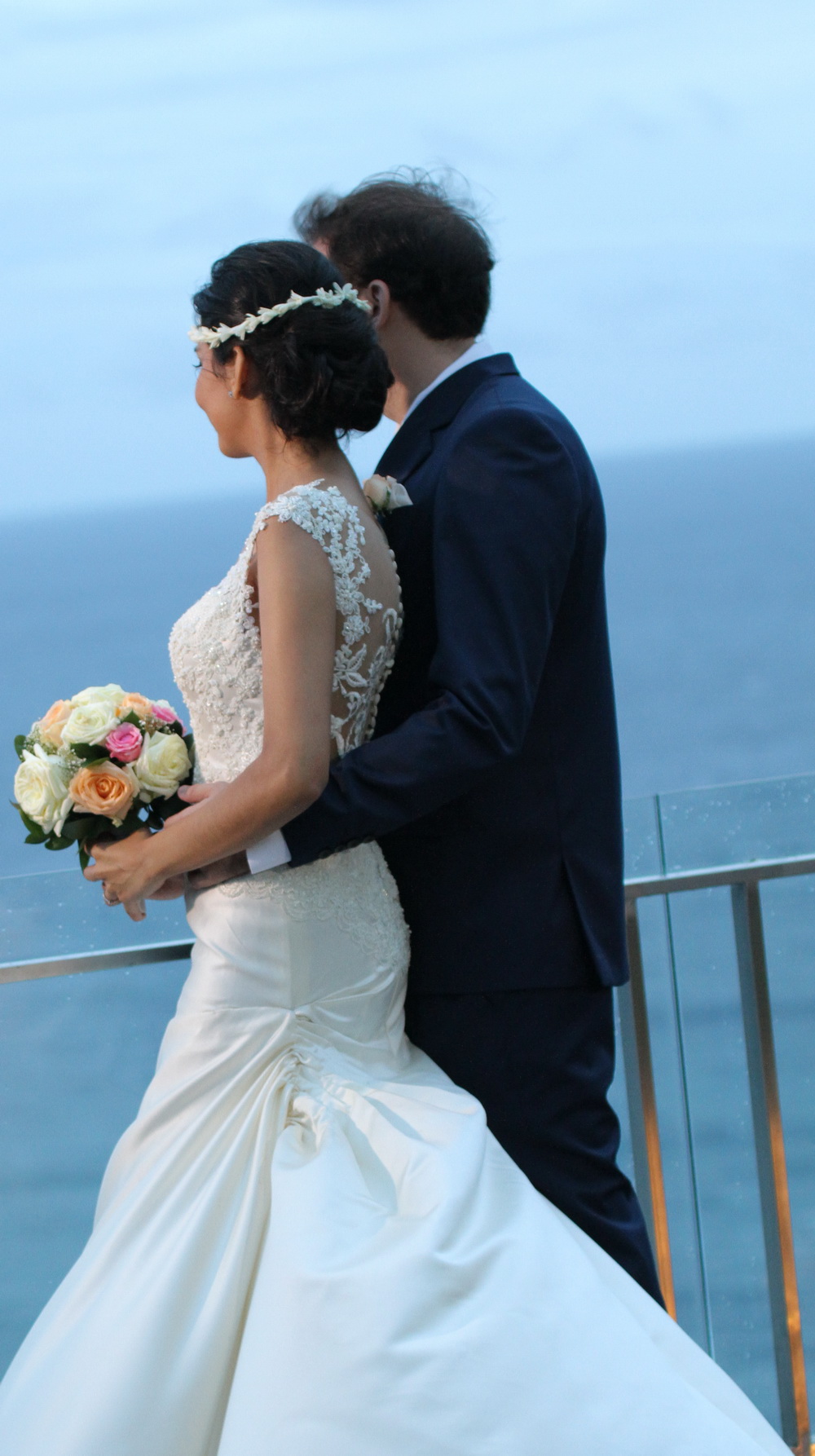 Pasangan pengantin mengenakan Jas dan Wedding Dress karya Fifilia, berpose di lokasi wedding dekat tepi laut di Bali.